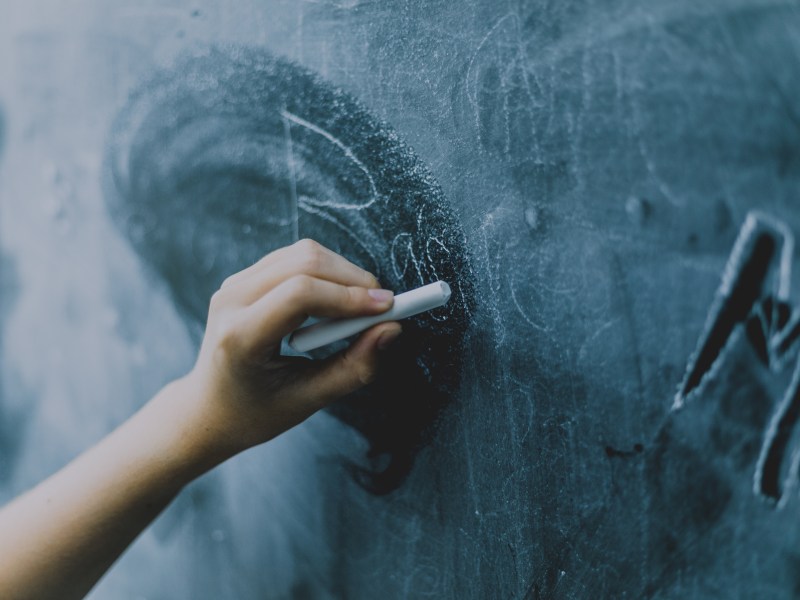 A young person's hand writes on a chalkboard.