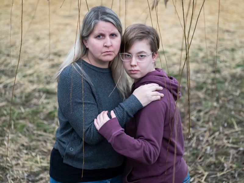 Lisa Norris stands hugging her daughter Hannah. Lisa has long blond hair and is wearing a blue sweater. Hanna has short brown hair and wears glasses and a purple hoodie.