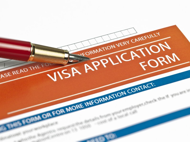 The top of a printed visa application can be seen. It says "Visa Application Form" at the top and below has contact information.